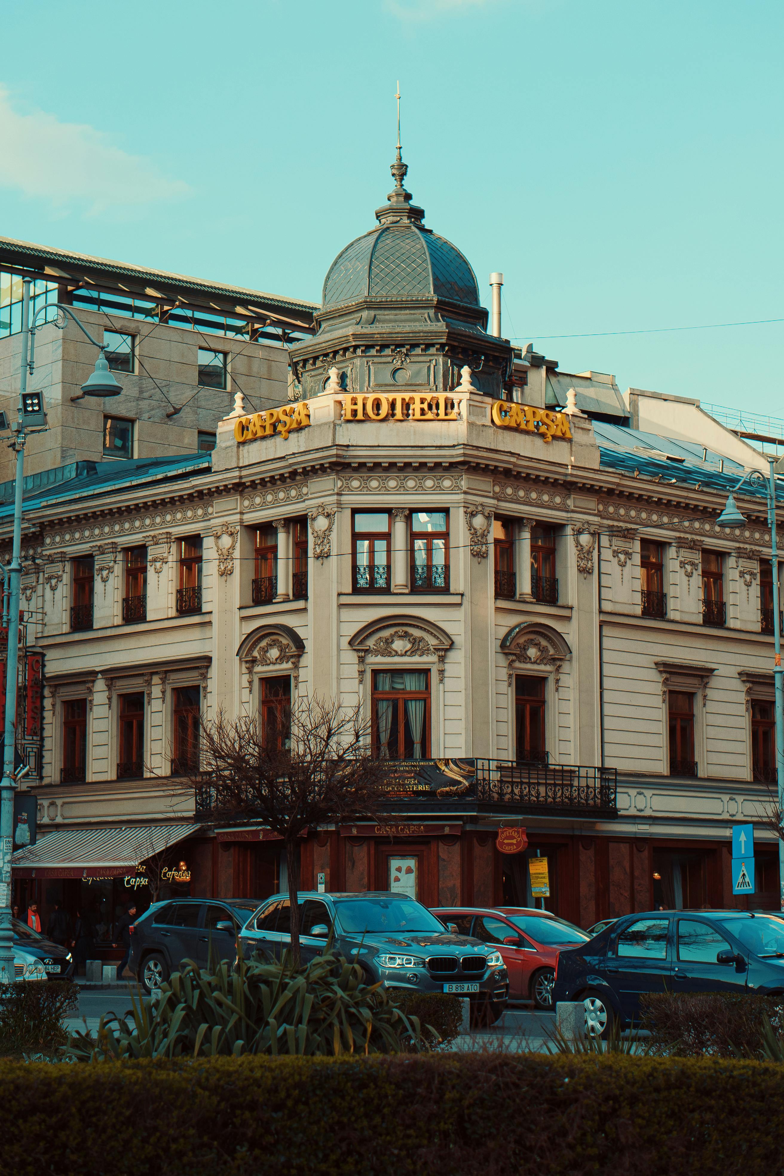 Free Elegant historic hotel facade on a city corner with parked cars, showcasing classic European architecture. Stock Photo