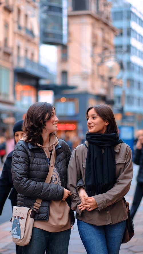 Free Two young women enjoying a casual stroll in a lively city street, smiling and talking. Stock Photo