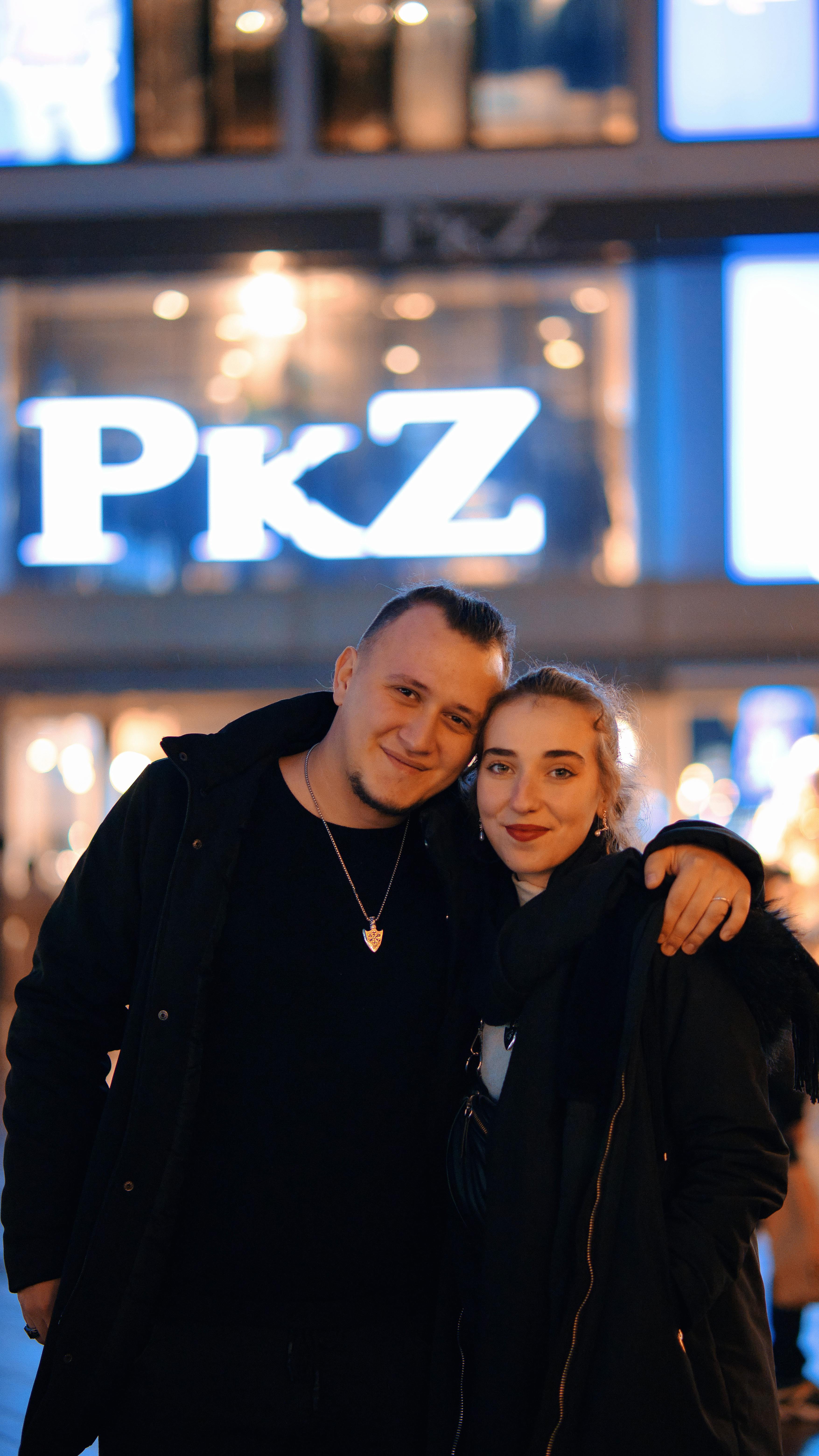 A smiling young couple embraces in a lively city street during a winter evening.