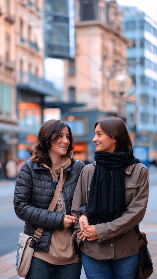 Free Two women enjoy a casual walk in a city, smiling with each other, showcasing casual fashion. Stock Photo
