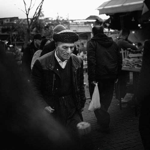 Free A senior man in a traditional hat walks through a bustling market in Sulaymaniyah, Iraq. Stock Photo