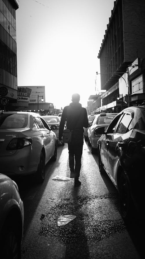 Silhouette of a Man Walking on a Street between Cars 