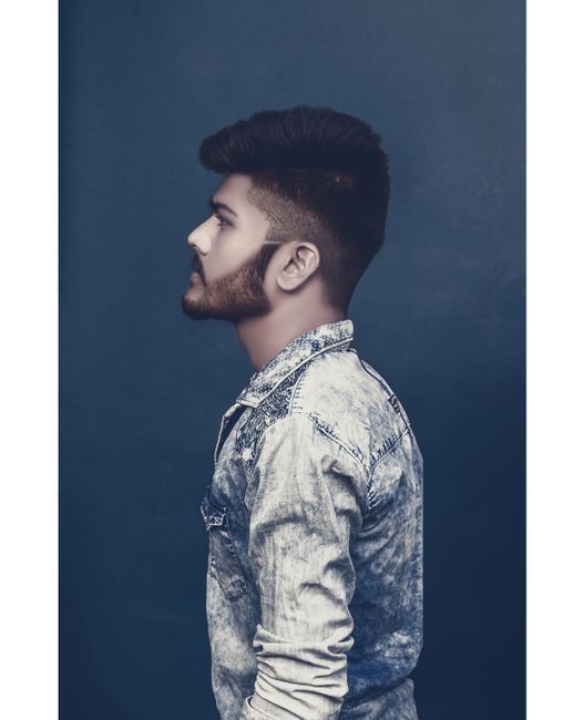 Studio portrait of a young man in a denim shirt with a trendy haircut and beard, posing in a side view.