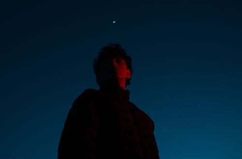 Free Dramatic low-angle photo of a man silhouetted against a starry night sky with the moon. Stock Photo