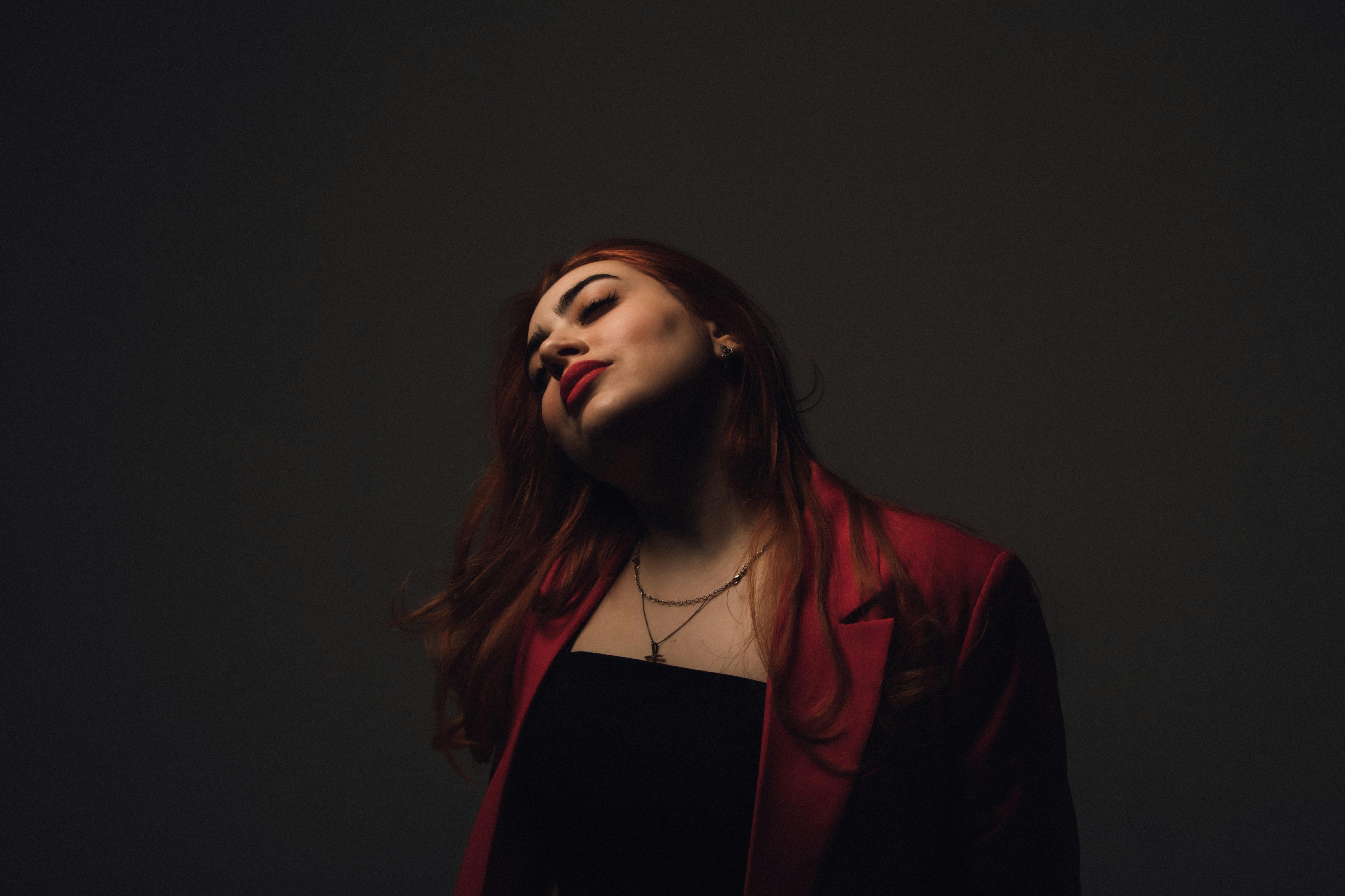 Elegant portrait of a redhead woman posing in a studio setting, wearing a stylish coat.