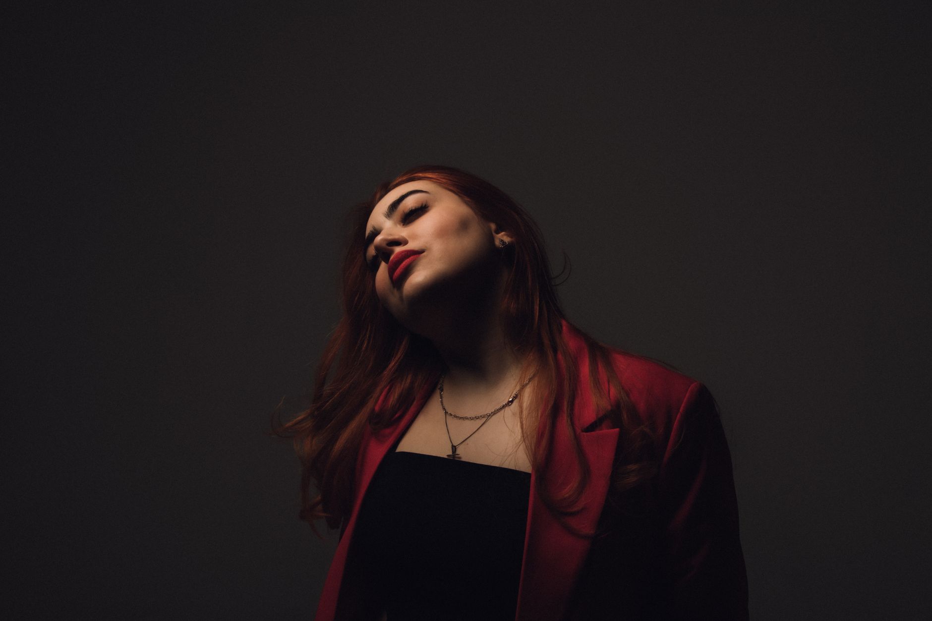 Elegant portrait of a redhead woman posing in a studio setting, wearing a stylish coat.