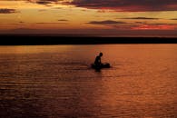 平静的水面上，日落时分，木筏上一个人的轮廓显得格外宁静