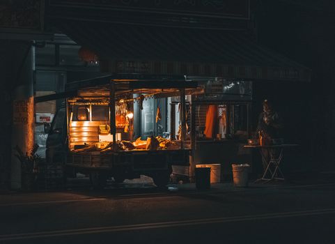A small food vendor truck on a dimly lit street selling meat at night.