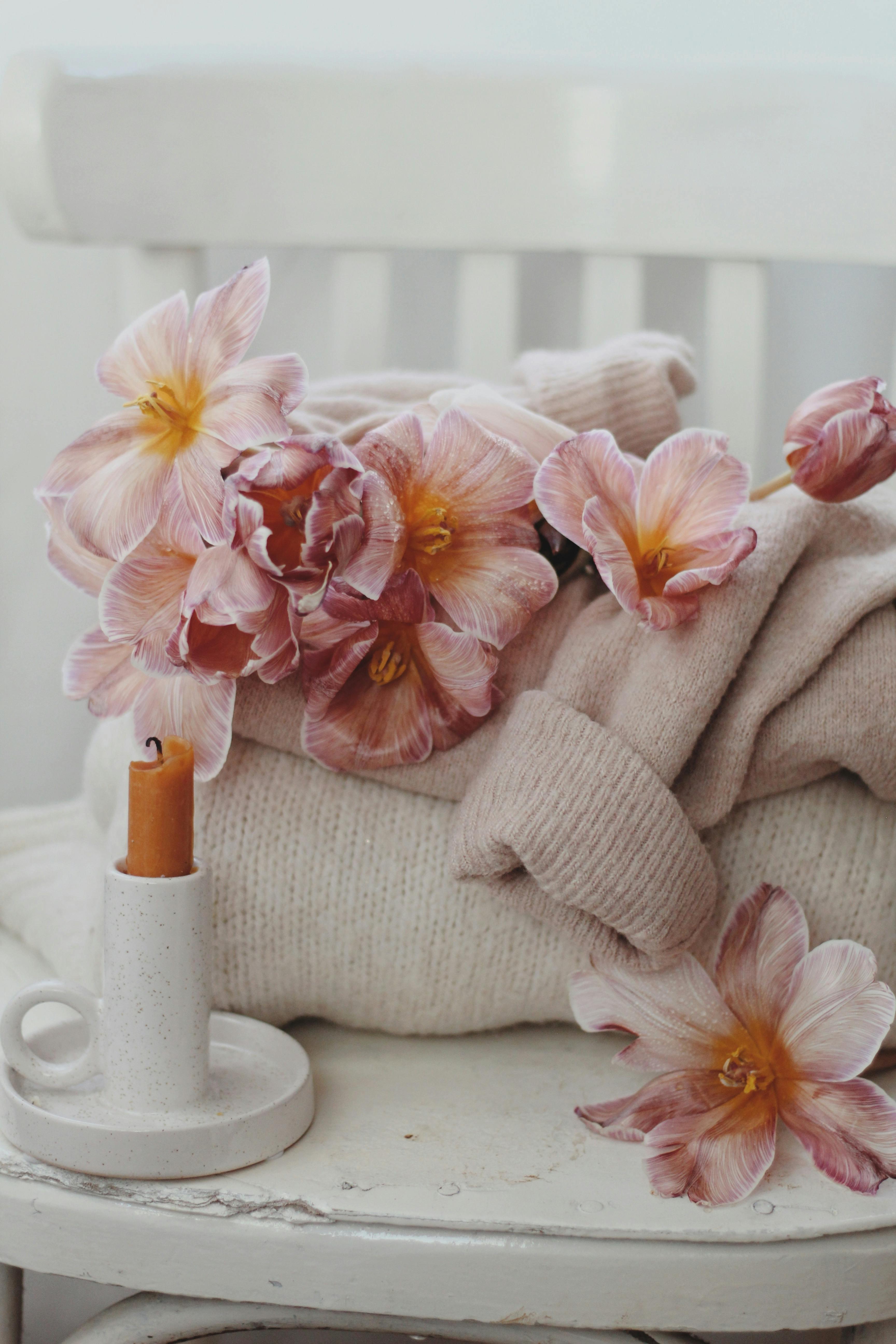 Soft pink flowers on a cozy sweater with a wax candle on a chair.