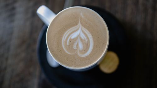 Free Top-down view of a cappuccino with intricate froth art in a white cup on a dark table. Stock Photo