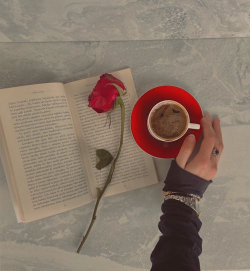 Woman Reaching for a Cup of Coffee next to a Book 