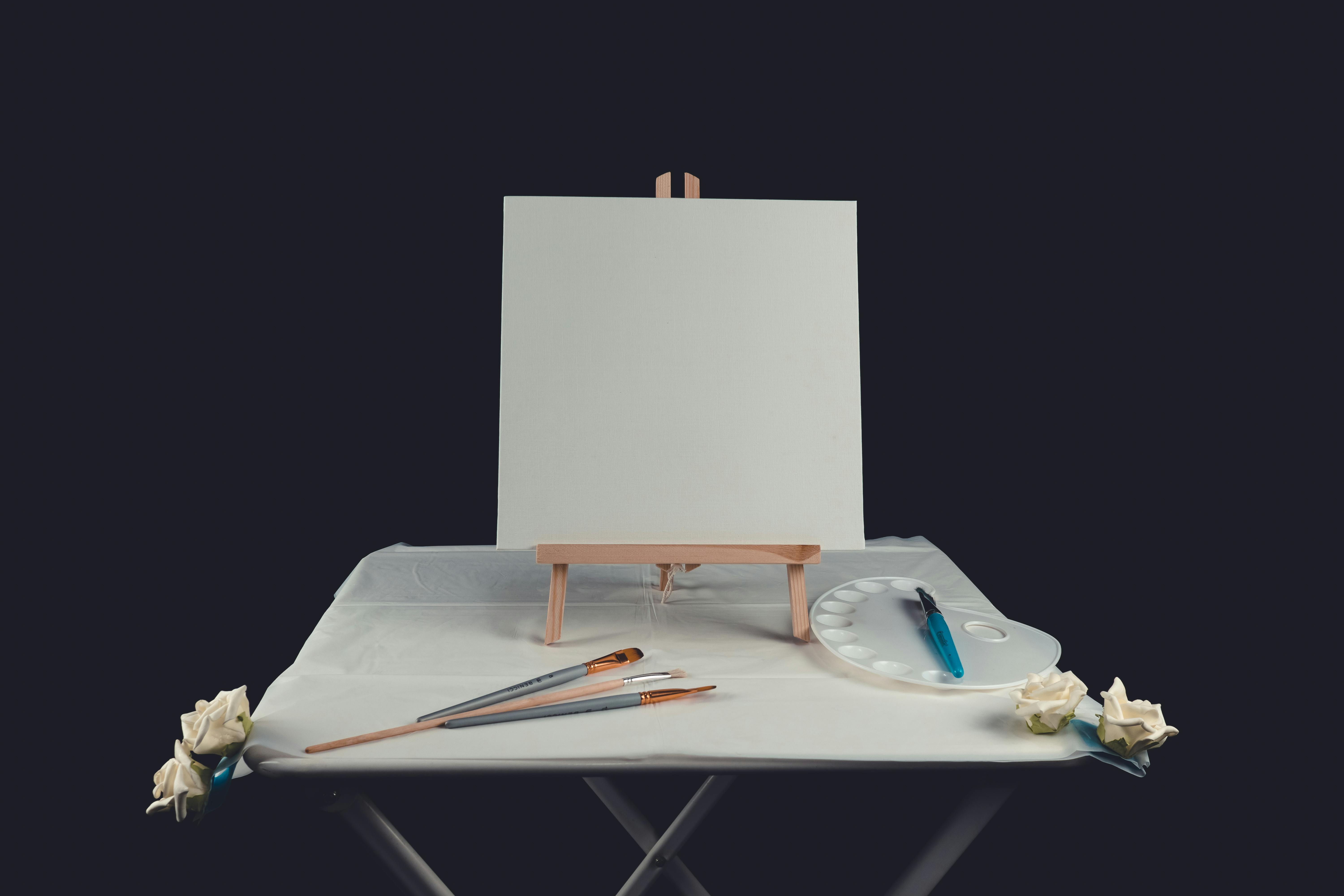 Artistic setup with blank canvas on a table surrounded by brushes and palette, inviting creativity.