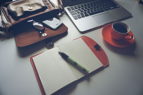 Free Stylish office workspace featuring a notebook, pen, laptop, and coffee cup on a tidy desk. Stock Photo