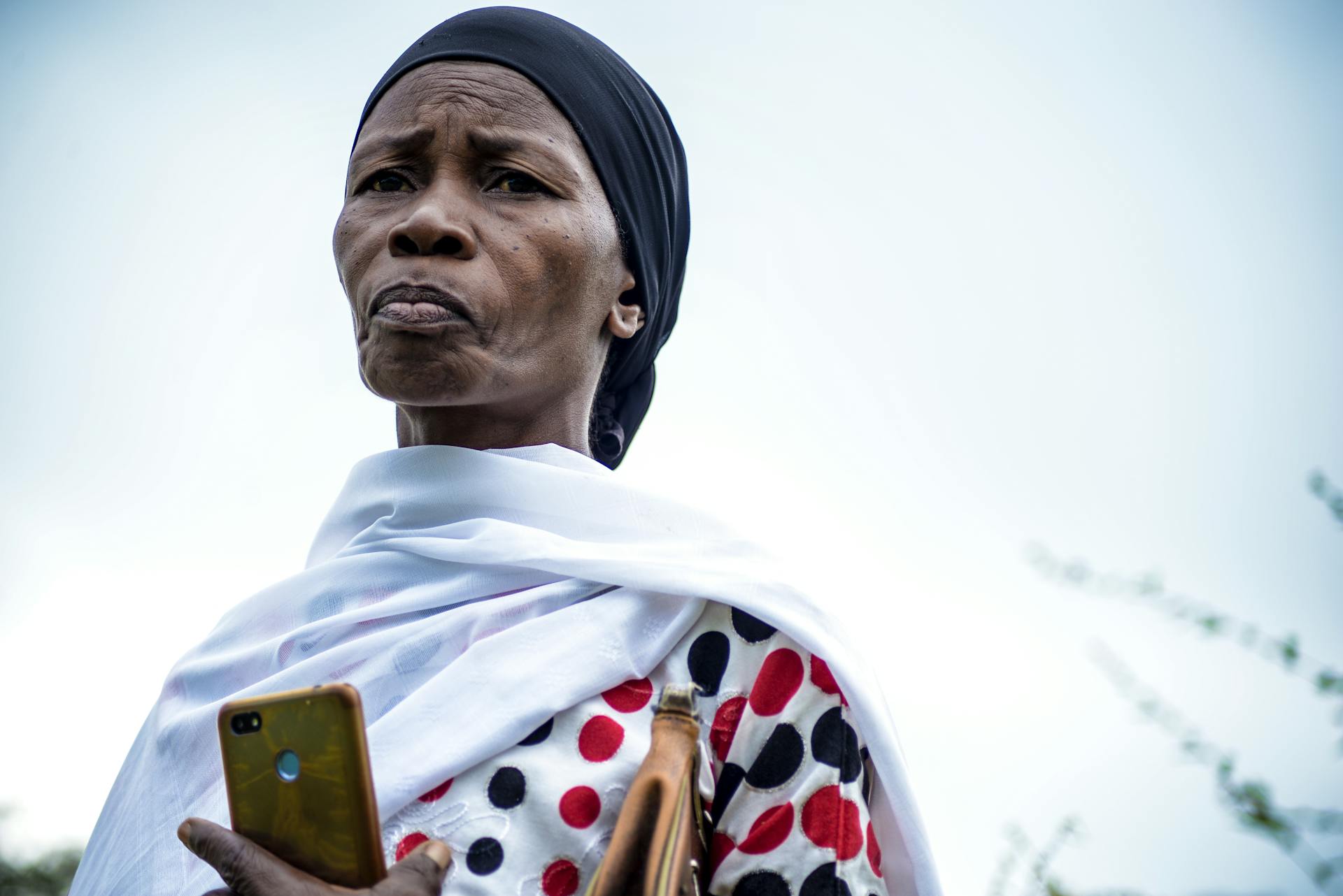 Portrait of a woman in traditional attire holding a smartphone outdoors in Tanzania.