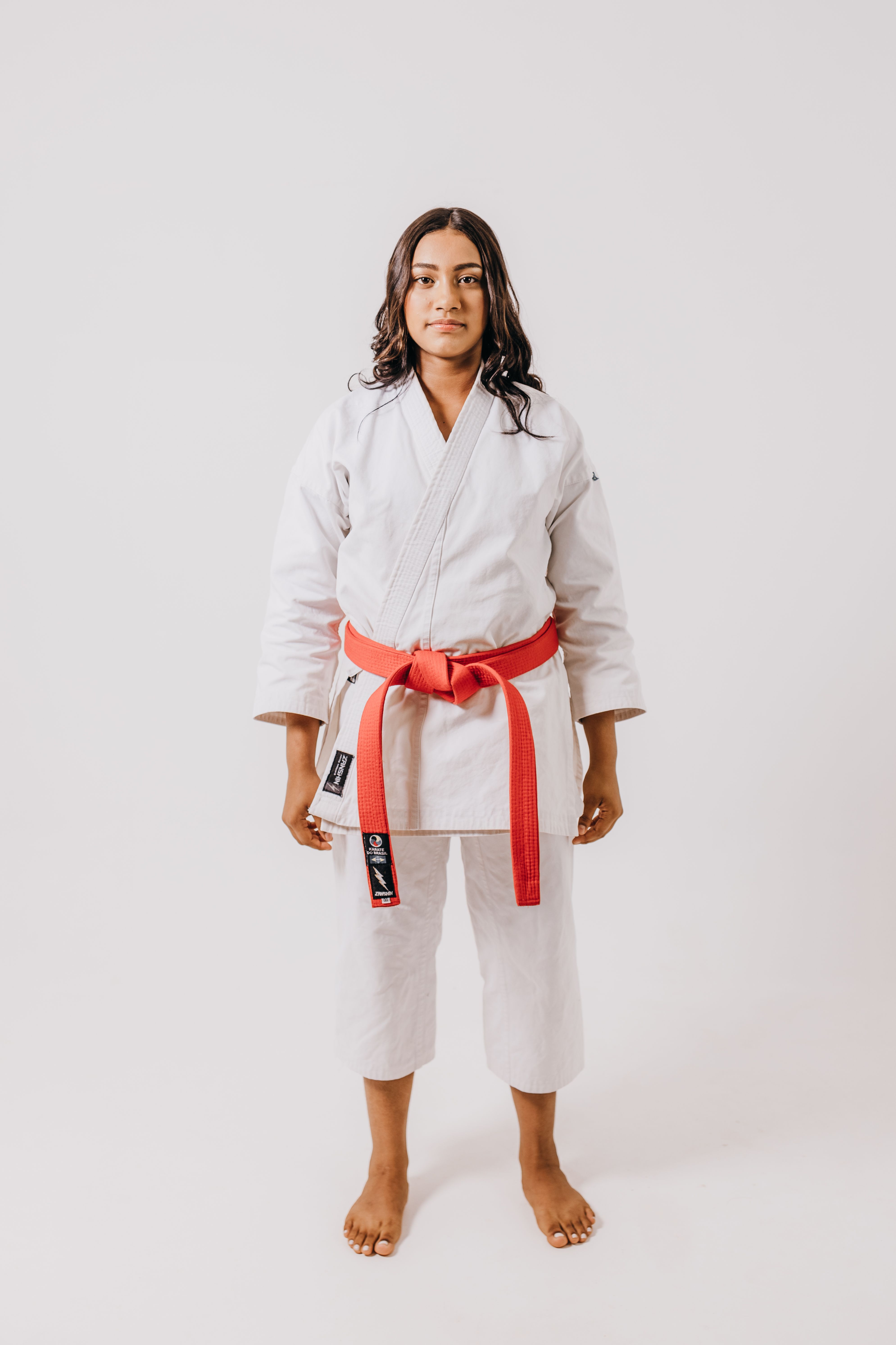 Studio shot of a teenage girl in white karate gi and red belt, symbolizing martial arts expertise.