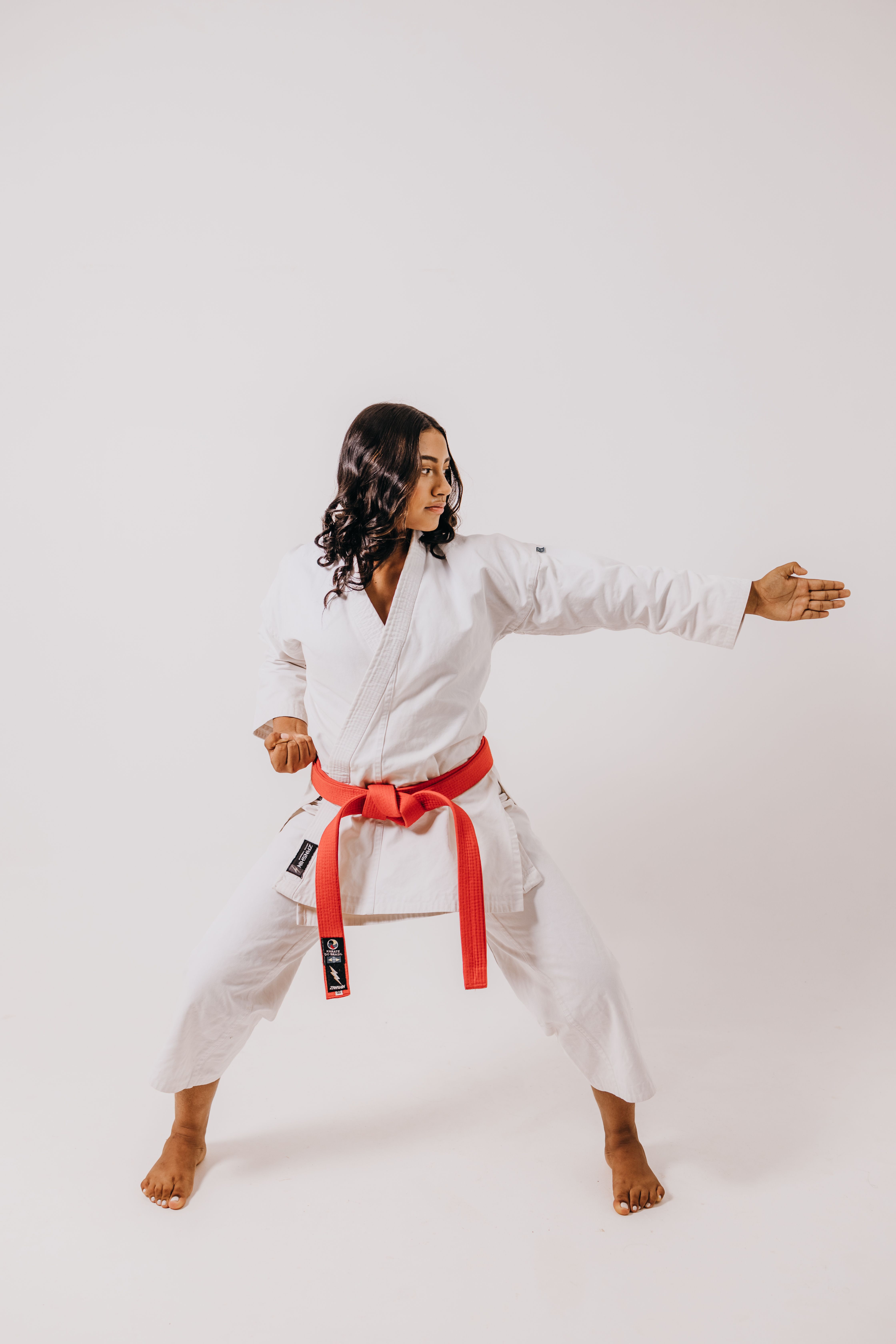 Karate practitioner in white gi and red belt performing pose in a studio setting.