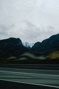A blurred view from a moving vehicle of distant snowy mountains under an overcast sky.