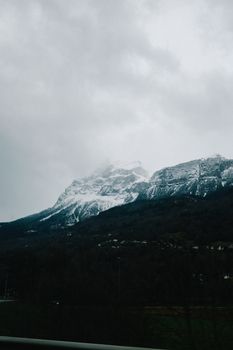 A scenic view of a snow-capped mountain partially obscured by clouds, creating a dramatic and moody landscape.
