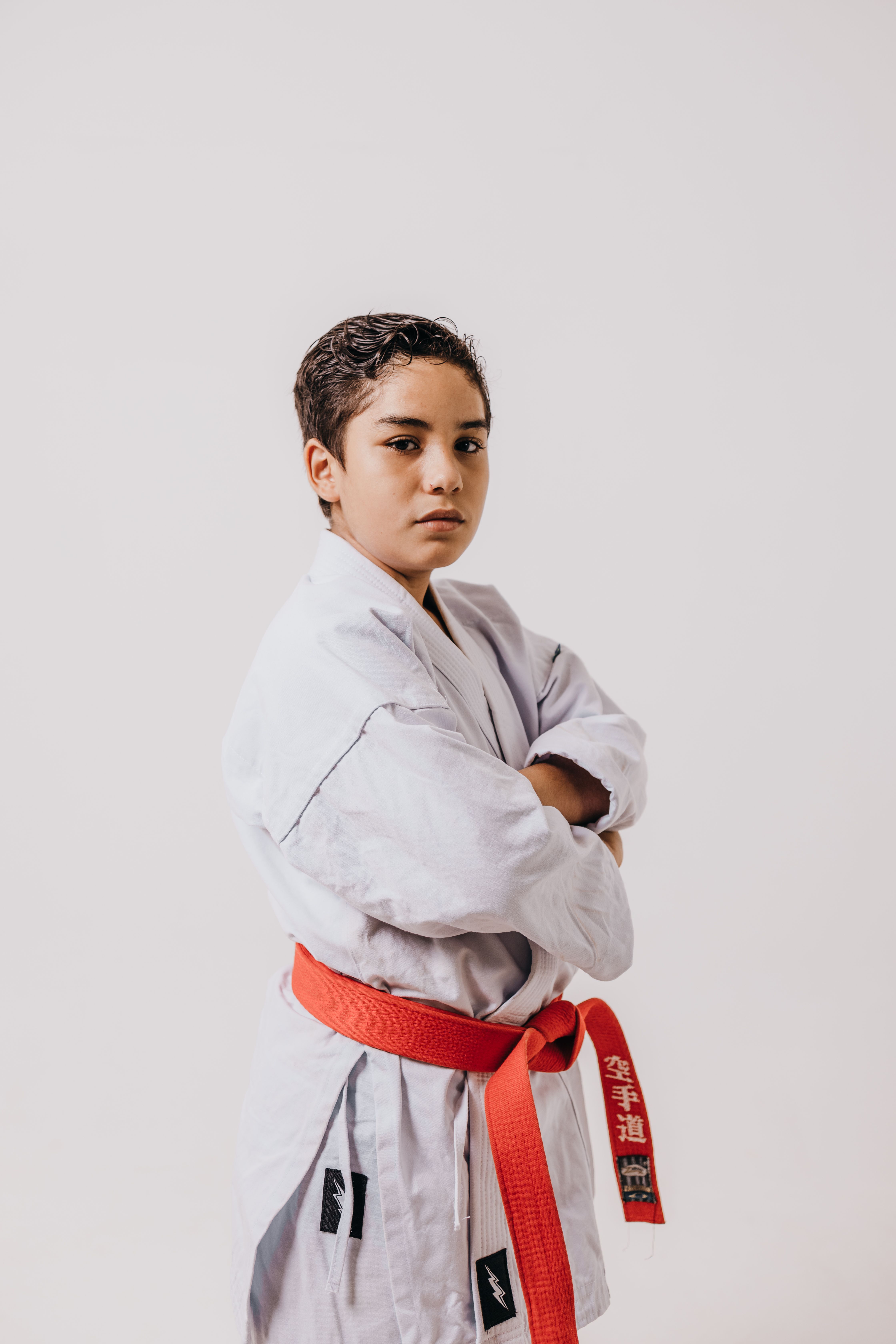 Teenager in karate gi and red belt posing confidently with arms crossed.