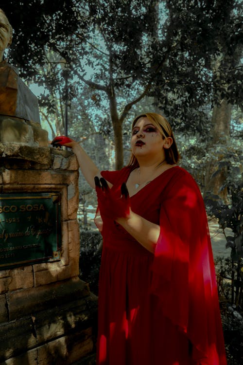 Woman in a Red Gown and Halloween Makeup Standing next to a Tombstone 