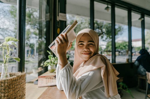 Chica Hijab Sonriente Disfrutando De Un Libro En Una Cafetería Acogedora En La Ciudad