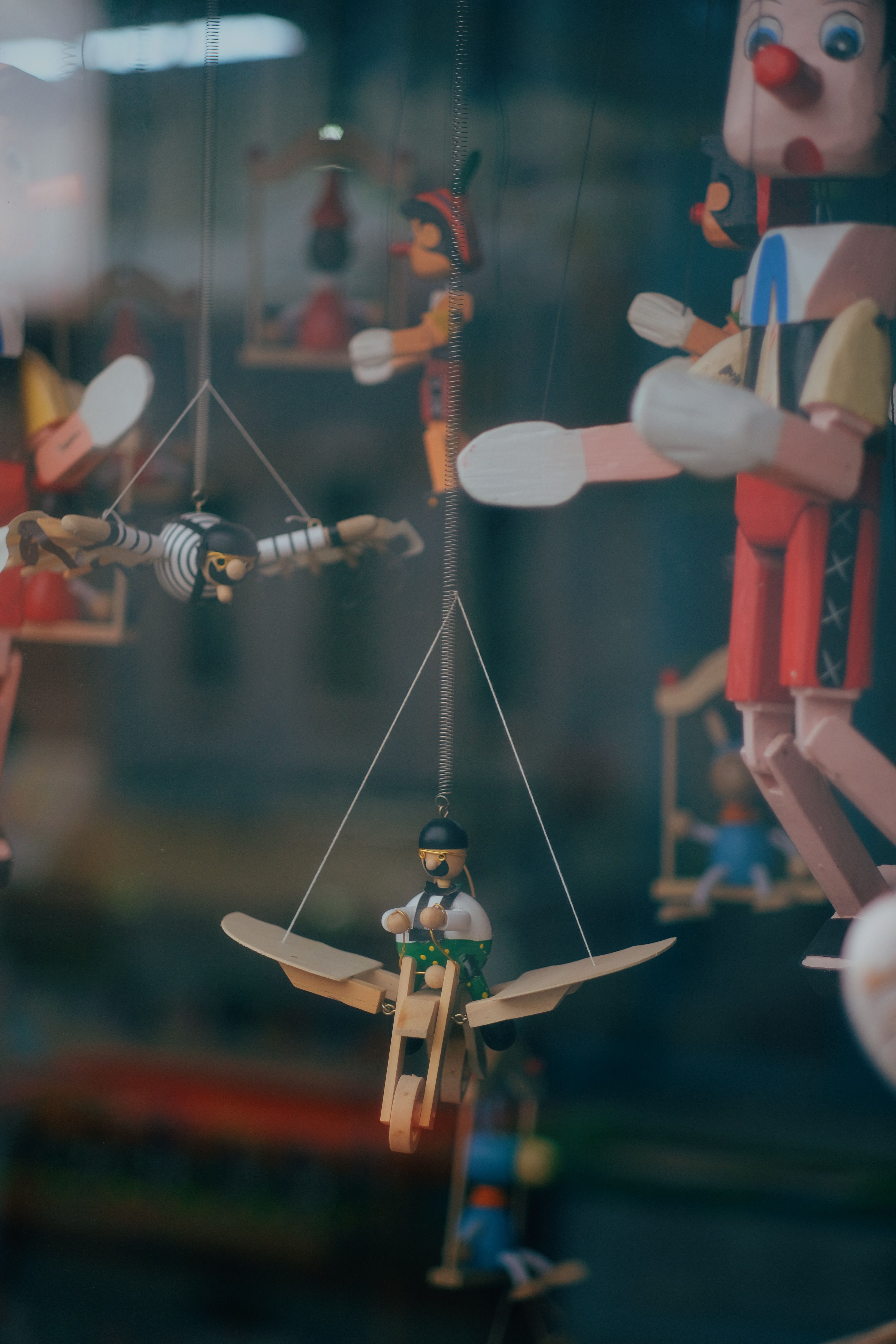 Charming display of handcrafted wooden marionette toys hanging inside a shop window.