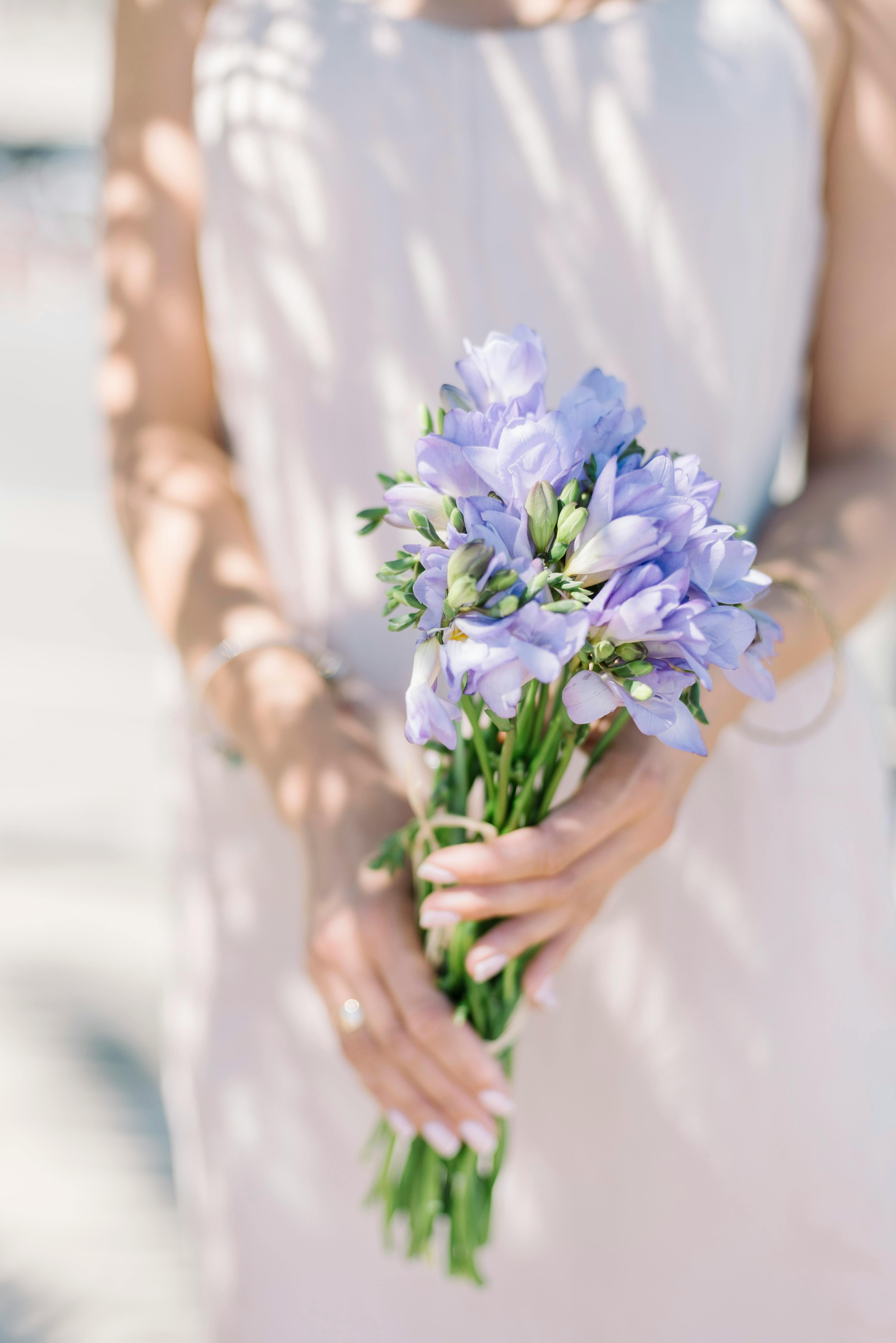 Elegant bouquet of delicate purple freesia held by a woman in a white dress, bathed in sunlight.