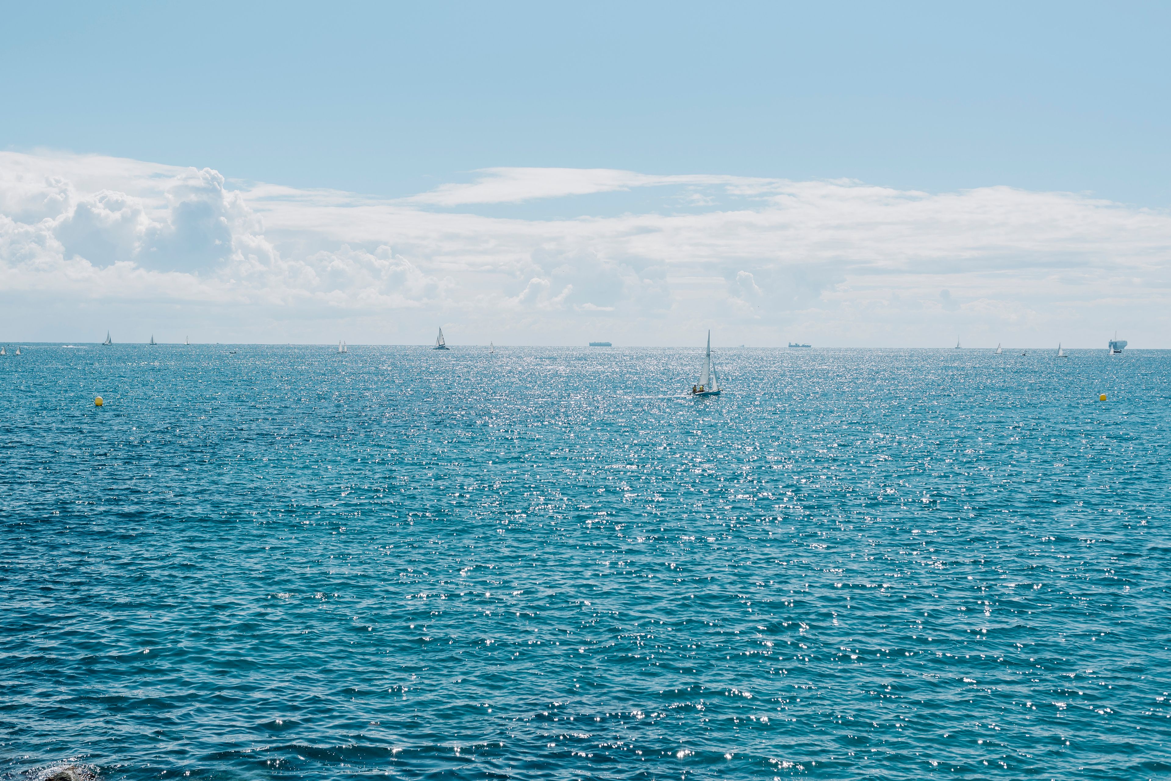 Sparkling blue ocean with sailboats on a sunny day and fluffy clouds in the sky.