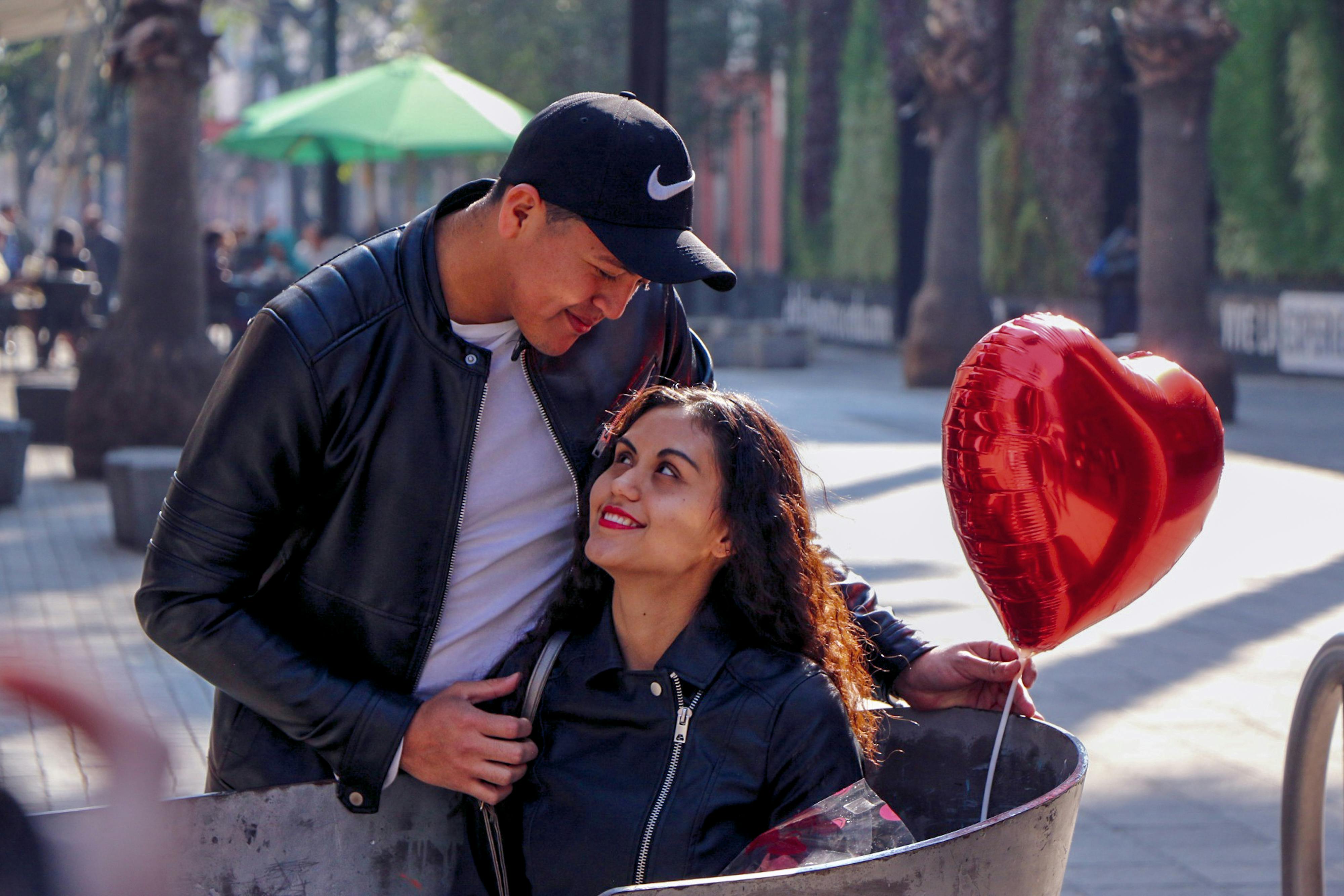 A smiling couple enjoys a romantic moment with a heart-shaped balloon in an outdoor setting.