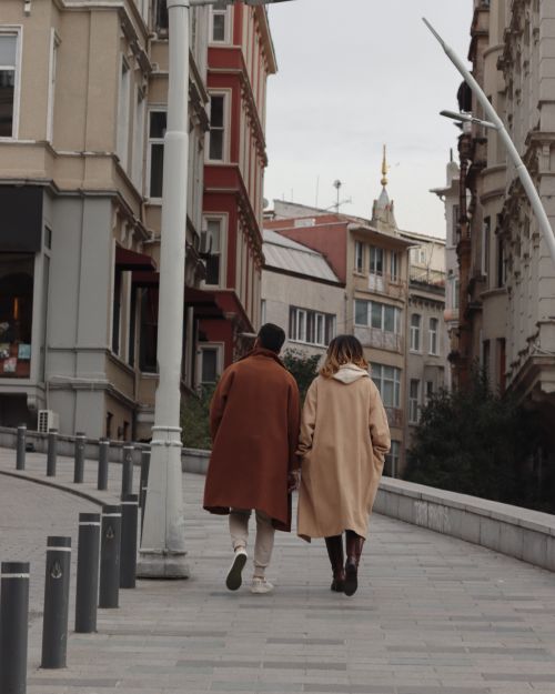 Free A couple in winter coats walking through a European city street with historical architecture. Stock Photo