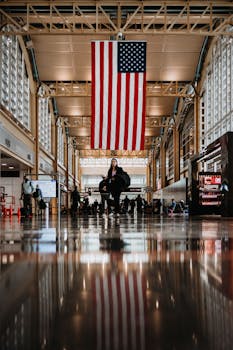 Travelers inside Washington DC's Reagan Airport beneath an American flag.