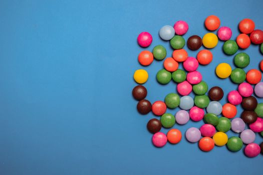 Vibrant multicolored candies scattered on blue background. Perfect for sweet-themed designs.