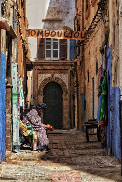 Free Man sitting in a narrow Essaouira alleyway. Sunlit streets, arches and colorful walls create a vibrant atmosphere. Stock Photo