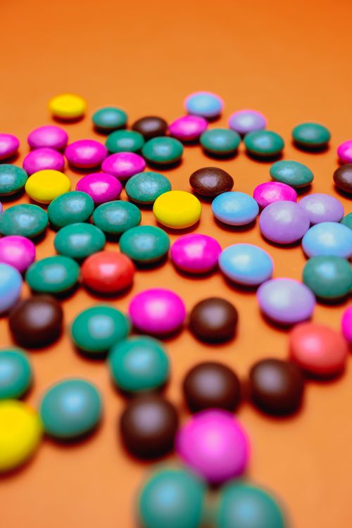 Free A vibrant collection of colorful candy coated chocolates on an orange background, creating an eye-catching still life. Stock Photo