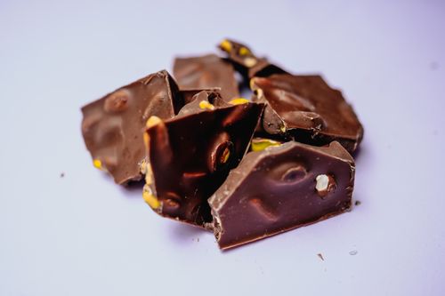 Free Close-up view of chocolate pieces with nuts on a purple background, perfect for food photography. Stock Photo