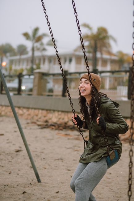 Woman enjoying a swing in a serene urban park on a cloudy day, exuding joy and leisure.