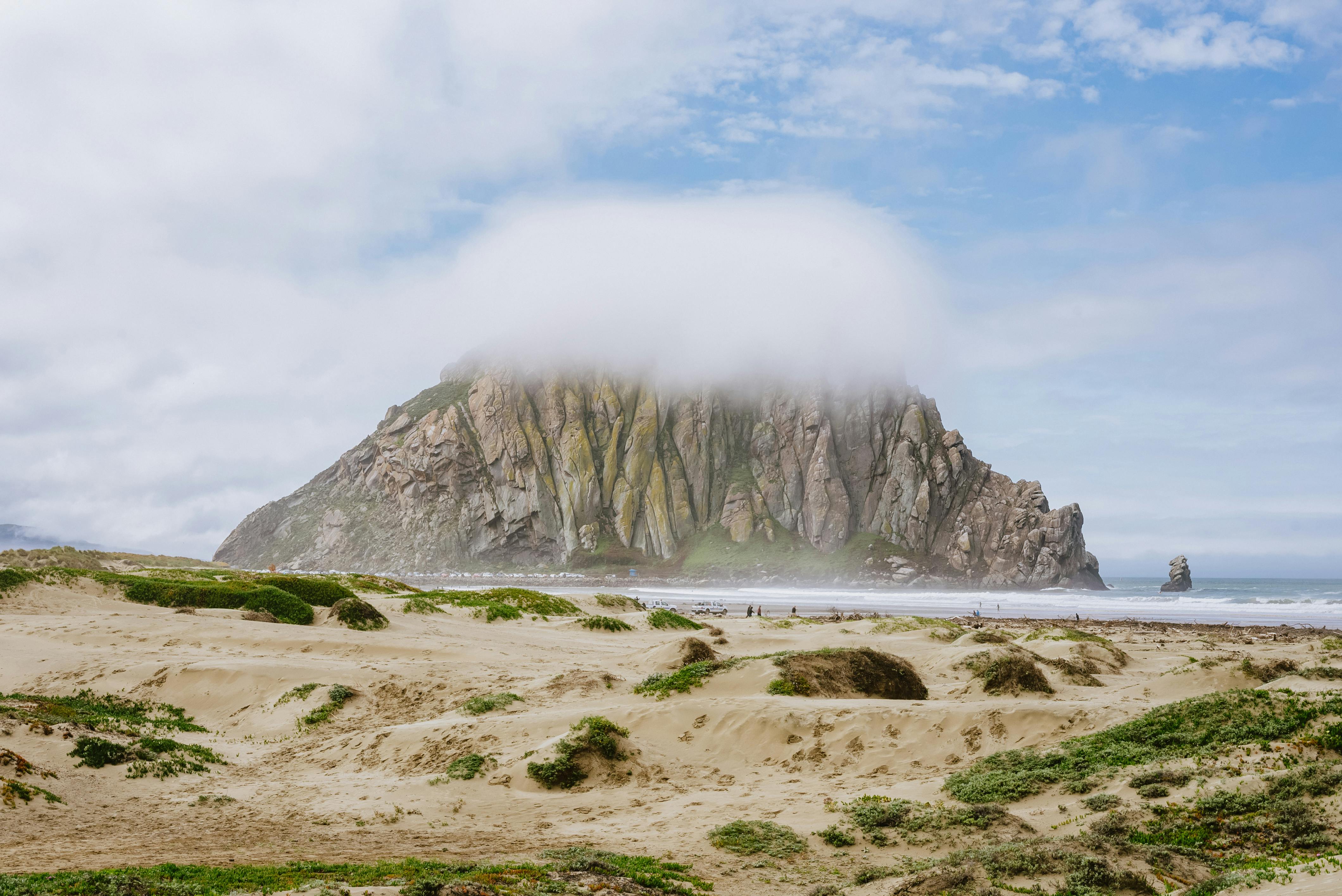 Morro Rock shrouded in fog with sandy beach and sea in Morro Bay, CA.