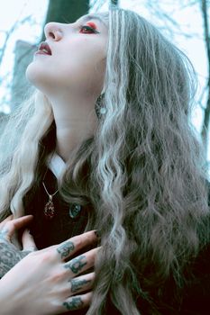Artistic portrait of a woman with tattoos and bold makeup looking upwards in a forest setting.