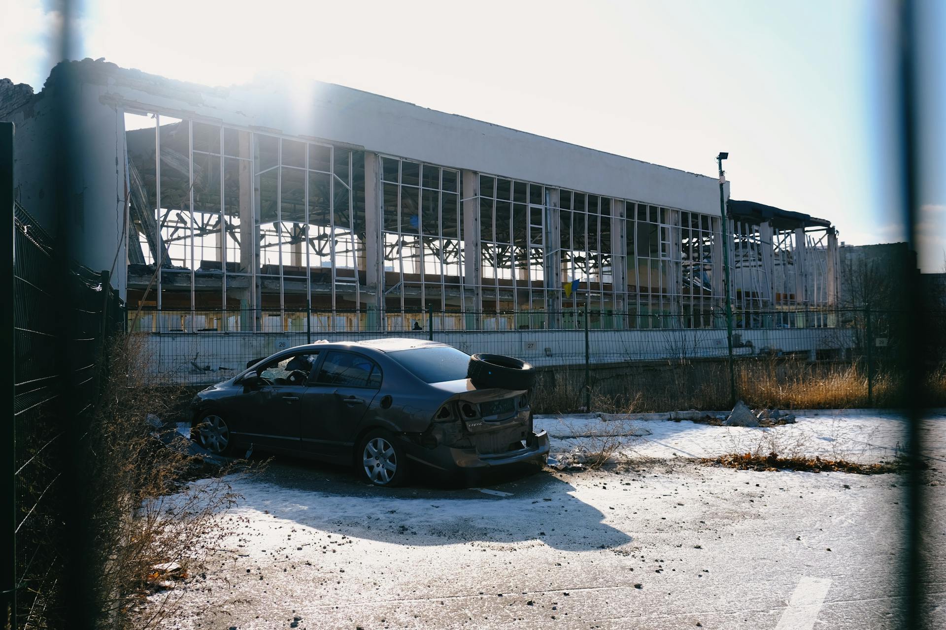 A sunlit abandoned factory with a wrecked car outside in Kharkiv, Ukraine.