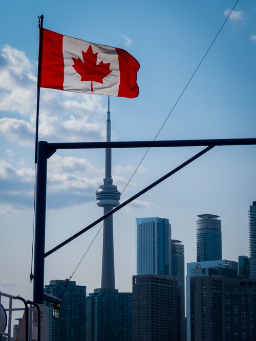 Free Canadian flag waves over Toronto skyline featuring the iconic CN Tower and skyscrapers. Stock Photo