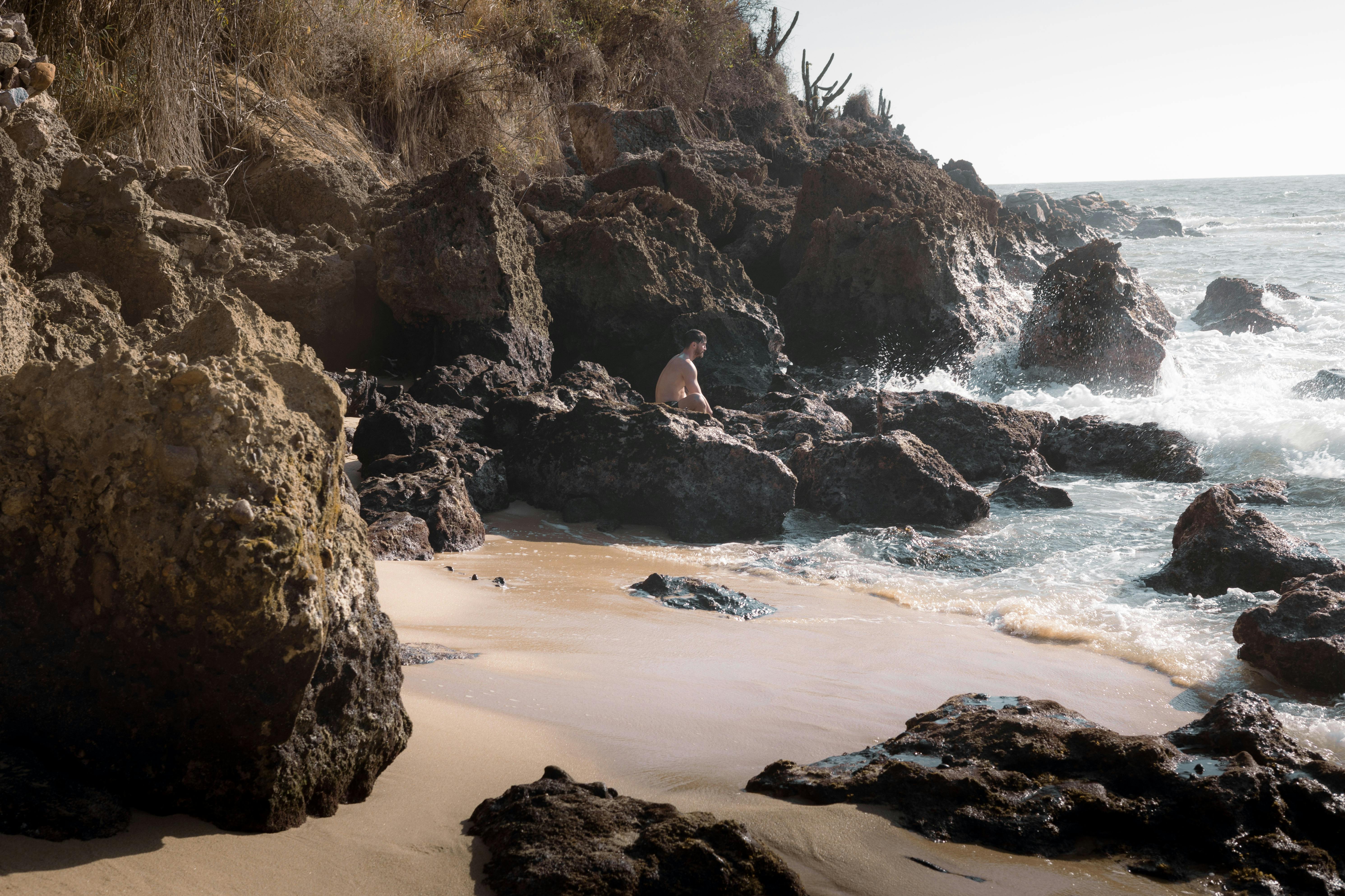 a person is sitting on the rocks near the ocean