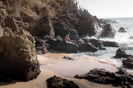 A lone person sitting on rocky cliffs by the ocean, capturing the serene and adventurous essence of a secluded beach.