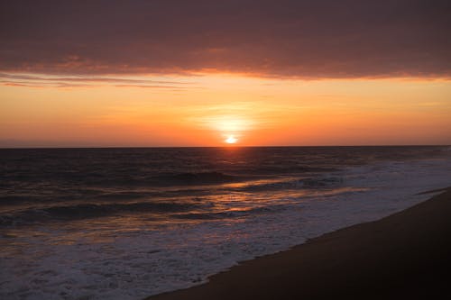 Free A sunset over the ocean with waves crashing Stock Photo