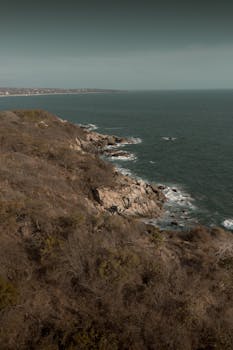 Dramatic view of rocky coastline and vast ocean in Puerto Escondido, Mexico, under daytime sky.