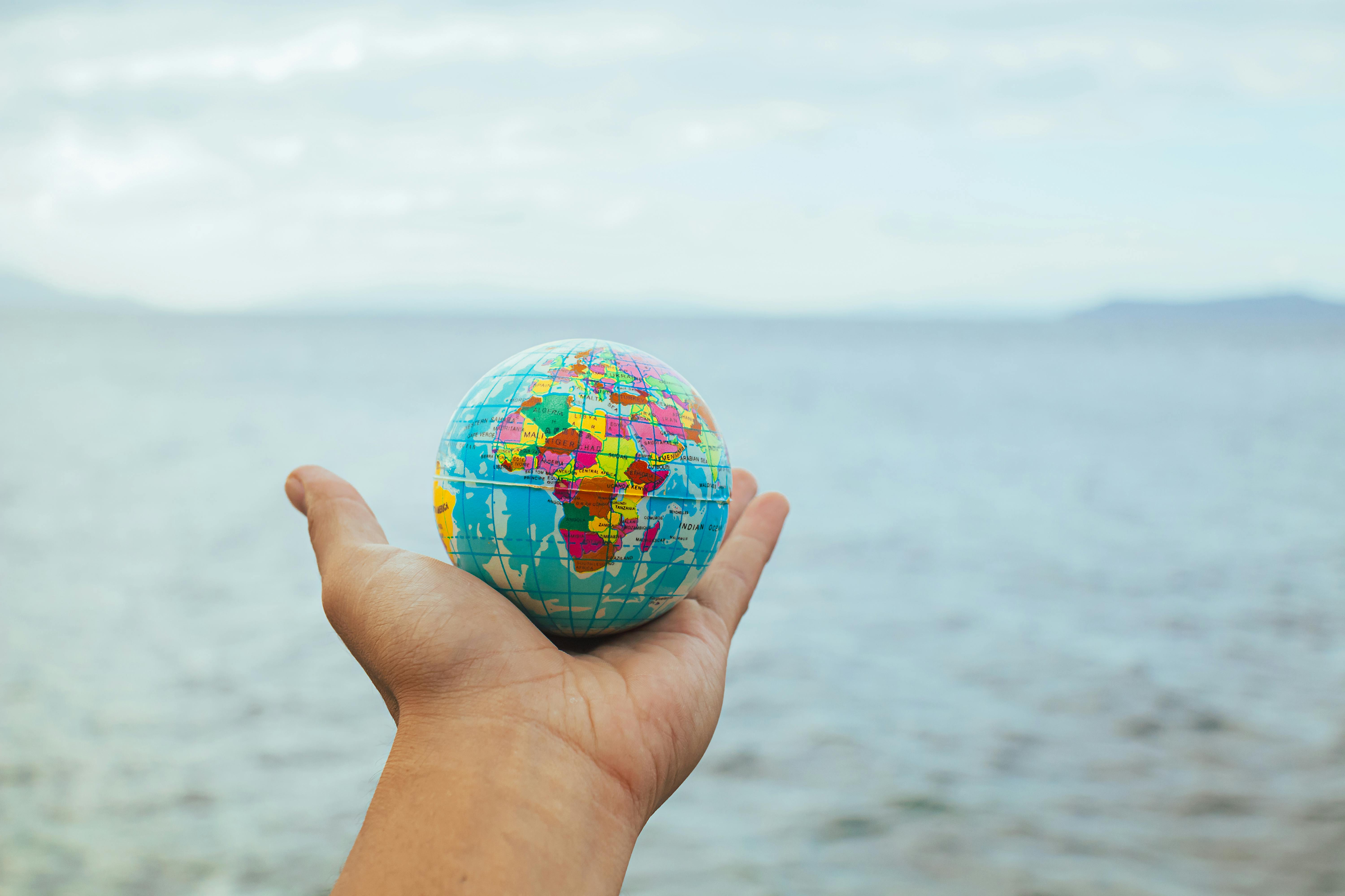A hand holding a small globe with an ocean backdrop, symbolizing global connection and travel.