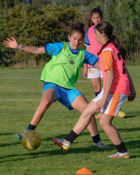 Three young women practicing soccer outdoors during a training session on a sunny day.