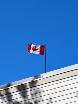 A Canadian flag waves on a rooftop against a bright blue sky in Halifax, NS, Canada.