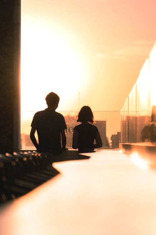 Free A silhouetted couple stands together at sunset in an urban location, creating a warm atmospheric scene. Stock Photo