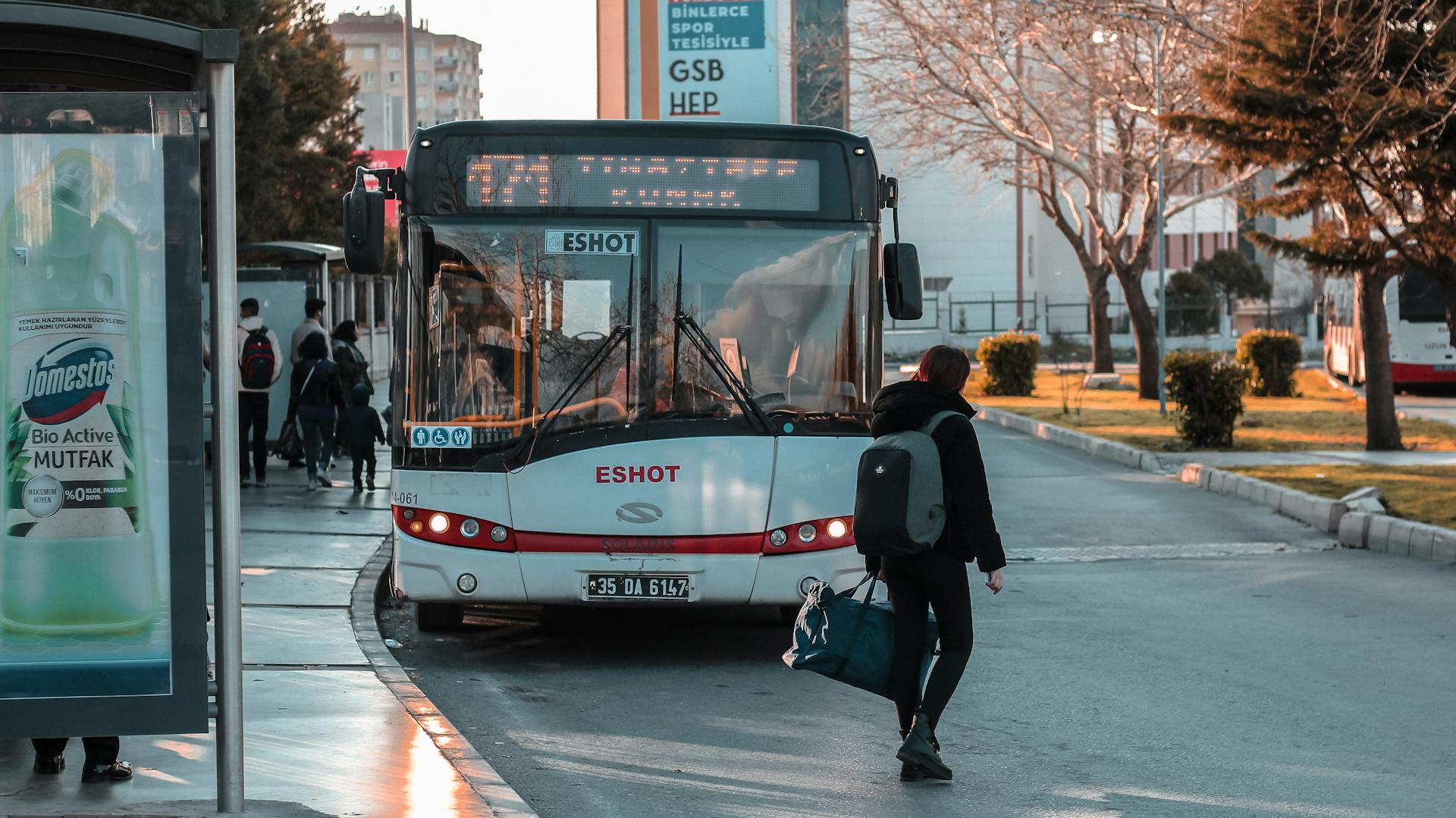 A person with a backpack boards a Solaris bus at an Izmir bus stop during the day.