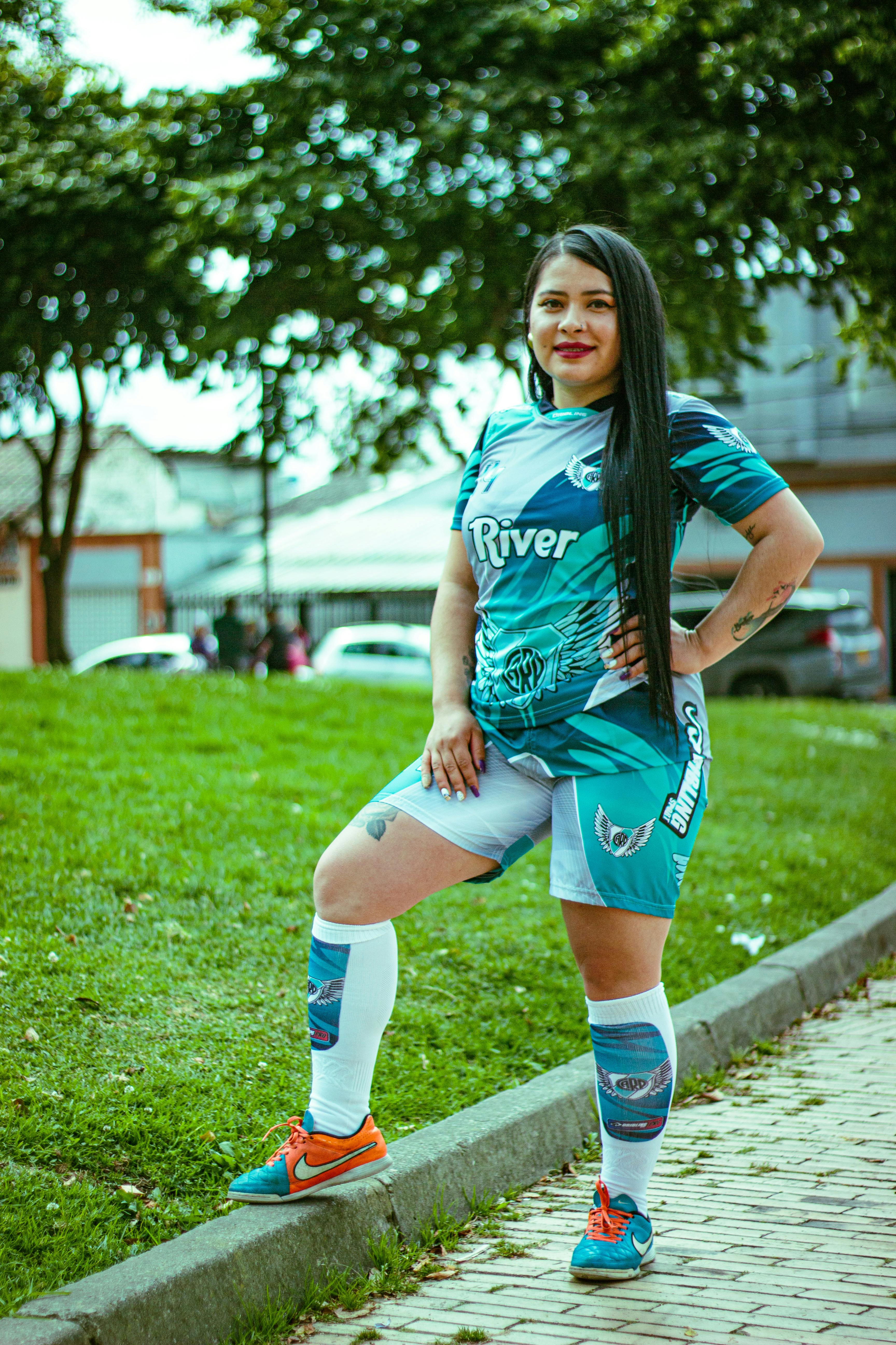 A woman in sports attire confidently poses outdoors on a sunny day.